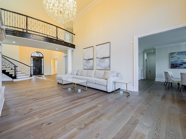 living room featuring a high ceiling, crown molding, a chandelier, light wood-type flooring, and decorative columns