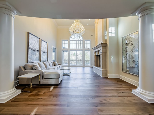 living room with dark wood-type flooring, an inviting chandelier, crown molding, a towering ceiling, and ornate columns