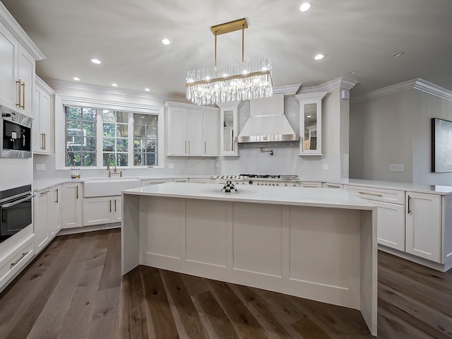 2748 Turtle Lake Dr, Bloomfield Hills, MI 48302 - kitchen with wall chimney range hood, ornamental molding, a sink, white cabinetry, and a kitchen island