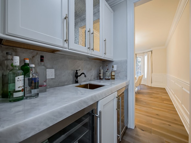 bar featuring sink, light stone counters, light hardwood / wood-style floors, white cabinets, and ornamental molding