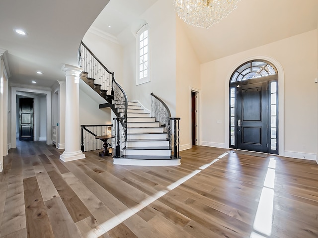 foyer entrance featuring ornate columns, a high ceiling, a notable chandelier, hardwood / wood-style floors, and ornamental molding