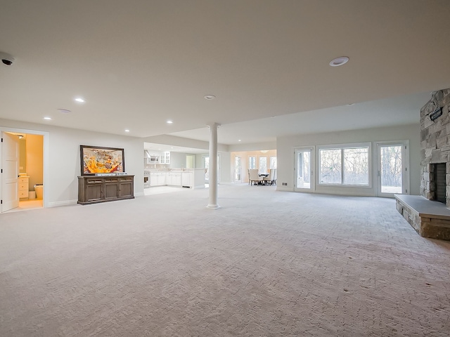 unfurnished living room featuring light carpet, decorative columns, and a stone fireplace