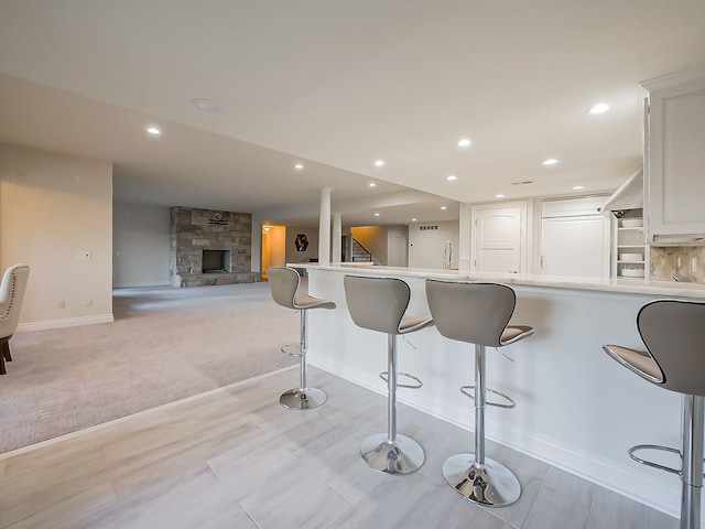 kitchen featuring light carpet, paneled refrigerator, a fireplace, a kitchen bar, and white cabinetry