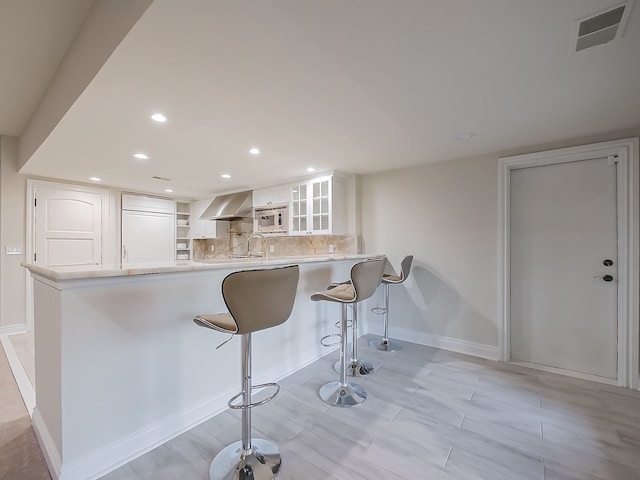 2748 Turtle Lake Dr, Bloomfield Hills, MI 48302 - kitchen with wall chimney exhaust hood, white cabinets, built in appliances, a breakfast bar area, and baseboards