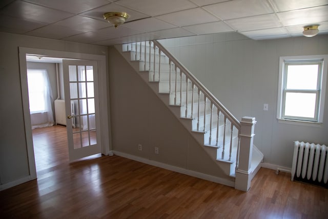 stairs featuring french doors, a drop ceiling, hardwood / wood-style flooring, and radiator