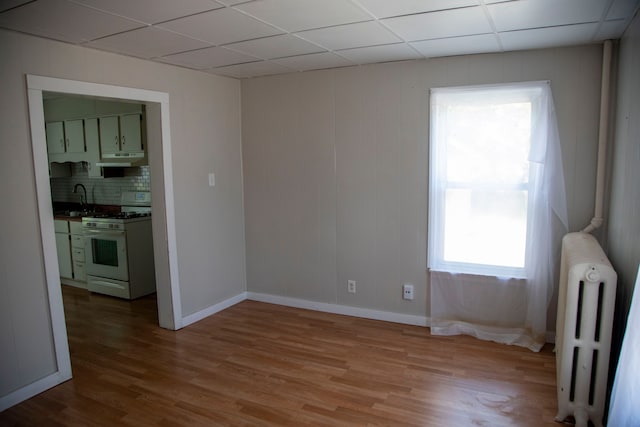 empty room featuring a drop ceiling, light hardwood / wood-style floors, sink, and radiator