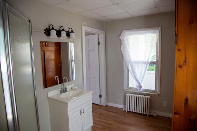 bathroom with radiator heating unit, vanity, wood-type flooring, and a drop ceiling