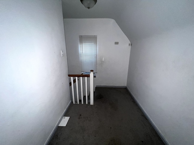 corridor with dark carpet and vaulted ceiling