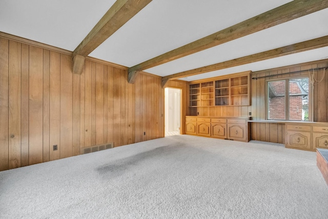 unfurnished living room with beam ceiling, carpet floors, and wood walls