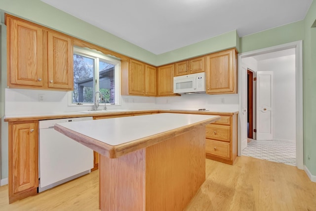 kitchen with a center island, white appliances, sink, light brown cabinetry, and light hardwood / wood-style floors