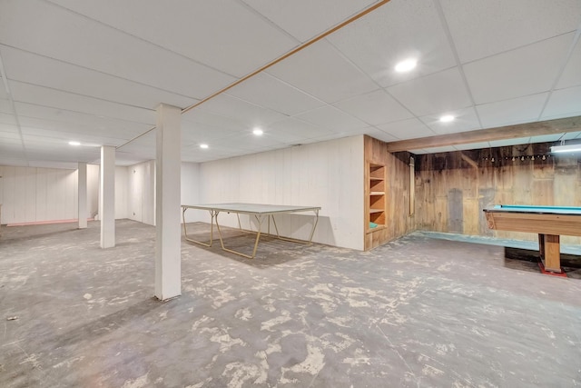 basement with a paneled ceiling, wooden walls, and billiards