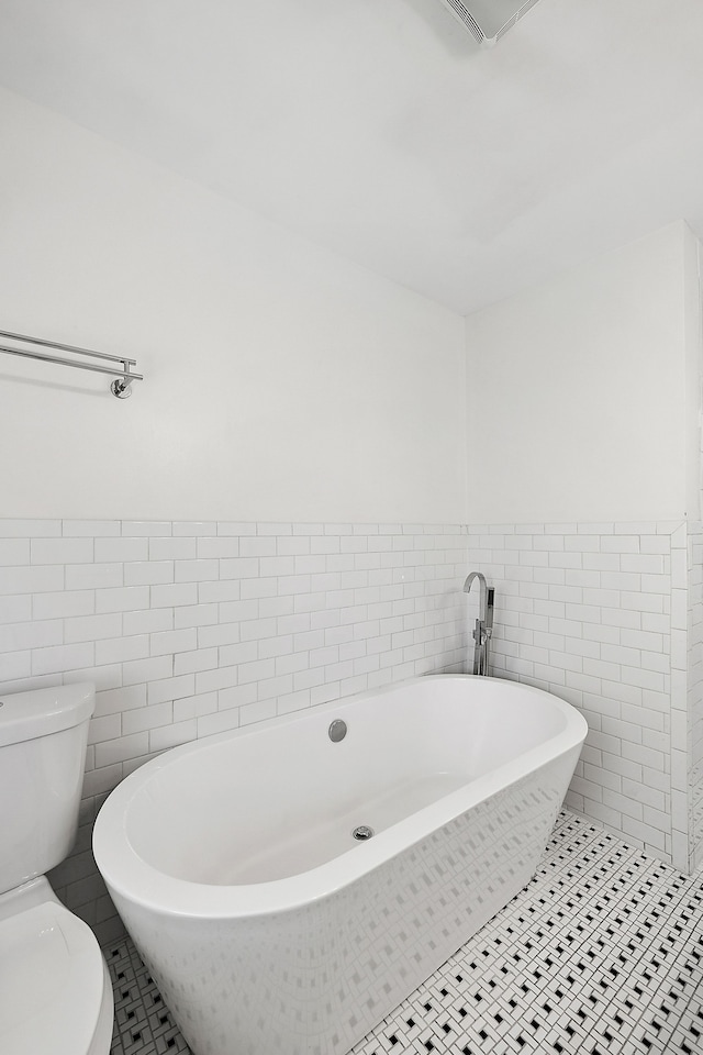 bathroom with tile patterned floors, a bathtub, tile walls, and toilet