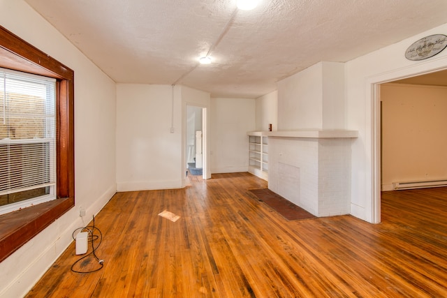 unfurnished living room featuring baseboard heating, a fireplace, hardwood / wood-style floors, and a textured ceiling