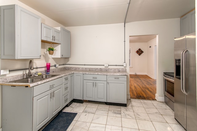 kitchen with gray cabinetry, sink, stainless steel appliances, and light hardwood / wood-style flooring