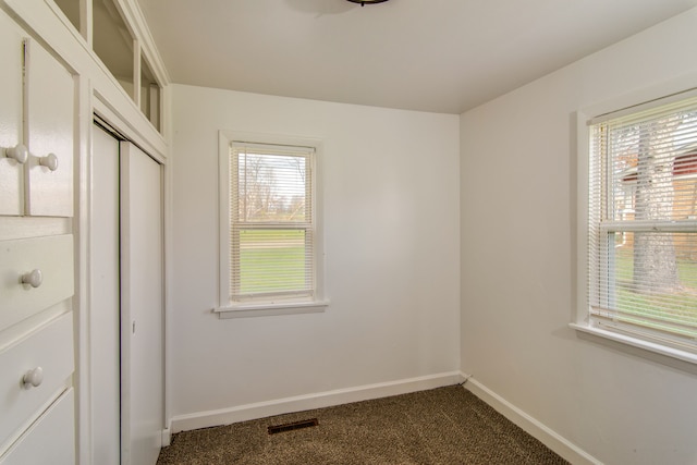 unfurnished bedroom featuring multiple windows, a closet, and dark colored carpet