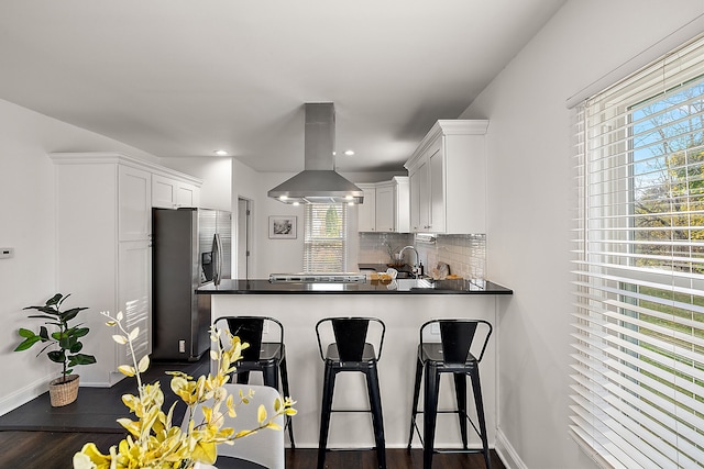 kitchen with stainless steel refrigerator with ice dispenser, island range hood, white cabinetry, and plenty of natural light