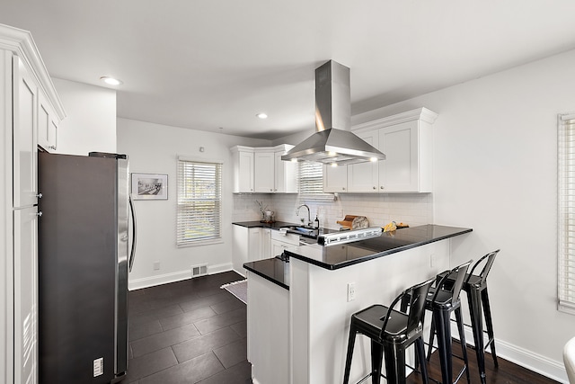 2552 Beals St, Detroit, MI 48214 - kitchen featuring freestanding refrigerator, island exhaust hood, dark countertops, a peninsula, and white cabinetry