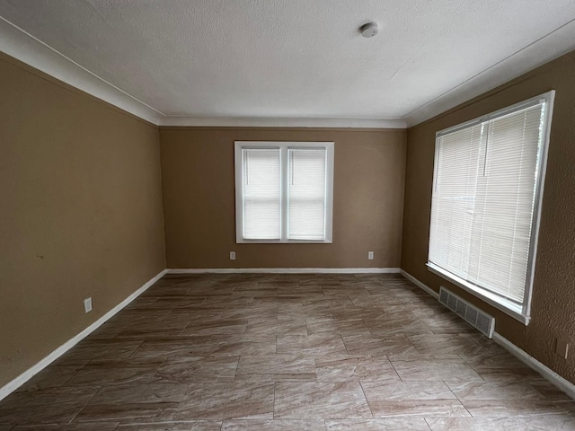 unfurnished room featuring crown molding, a textured ceiling, baseboards, and visible vents