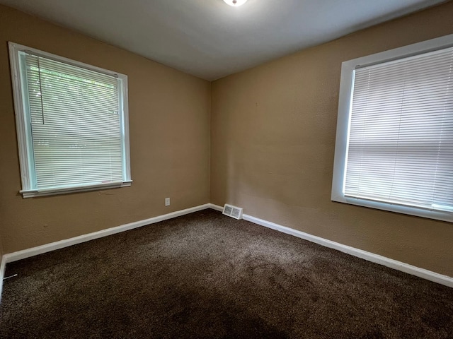 empty room featuring visible vents, baseboards, and dark colored carpet