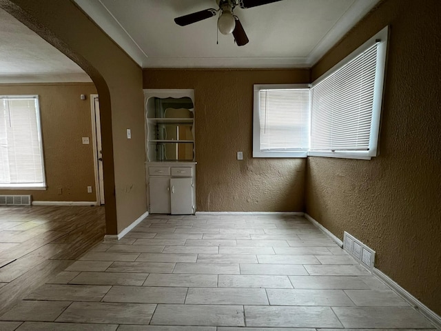 unfurnished room featuring a ceiling fan, visible vents, arched walkways, light wood-style floors, and a textured wall
