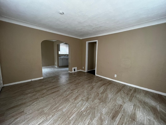 empty room with baseboards, arched walkways, wood finished floors, and visible vents