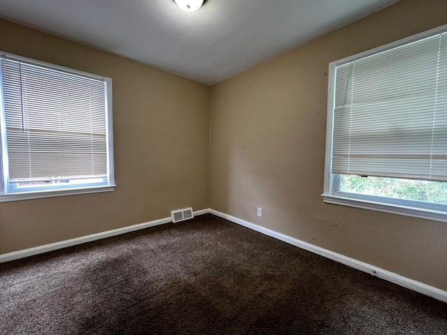 empty room featuring visible vents, baseboards, and dark colored carpet