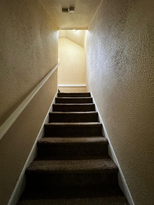 stairway with a textured wall and vaulted ceiling
