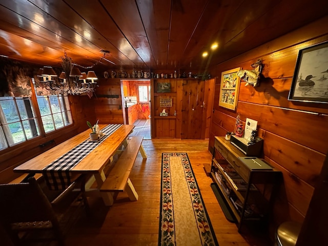 dining room featuring hardwood / wood-style flooring, wood walls, wood ceiling, and an inviting chandelier