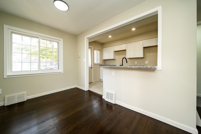 kitchen with light stone countertops, kitchen peninsula, dark wood-type flooring, sink, and white cabinetry