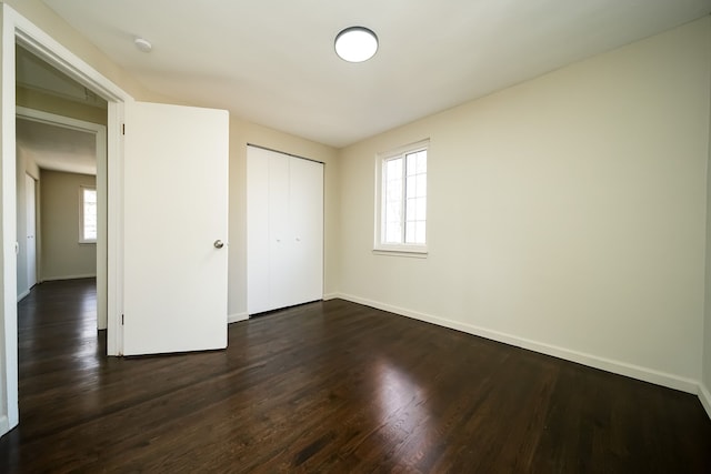 unfurnished bedroom with a closet, dark hardwood / wood-style floors, and multiple windows