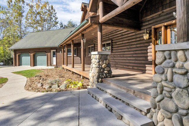 10560 Plaza Ct, Jerome, MI 49249 - view of side of home featuring log exterior, a garage, a porch, and concrete driveway