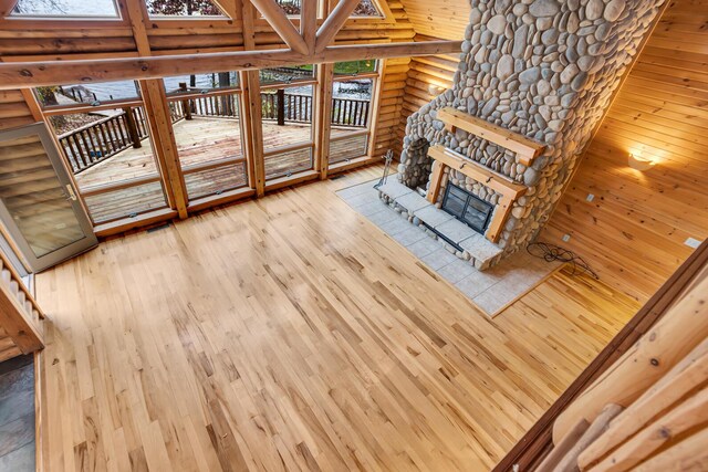 10560 Plaza Ct, Jerome, MI 49249 - unfurnished living room featuring log walls, high vaulted ceiling, wood-type flooring, a stone fireplace, and a skylight