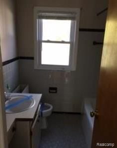 bathroom featuring vanity, toilet, and tile walls