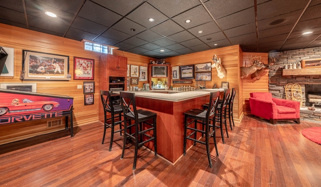 bar with wood-type flooring, a drop ceiling, and wooden walls