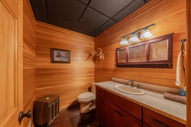 bathroom featuring vanity, wood walls, a drop ceiling, toilet, and wood-type flooring