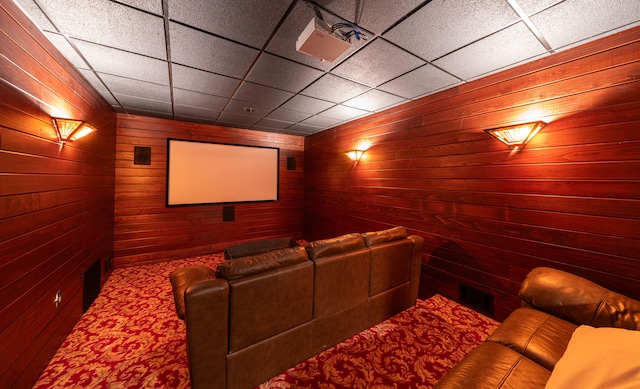 carpeted cinema room featuring a paneled ceiling and wooden walls