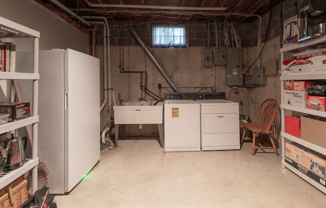 basement featuring washer and dryer, electric panel, white fridge, and sink