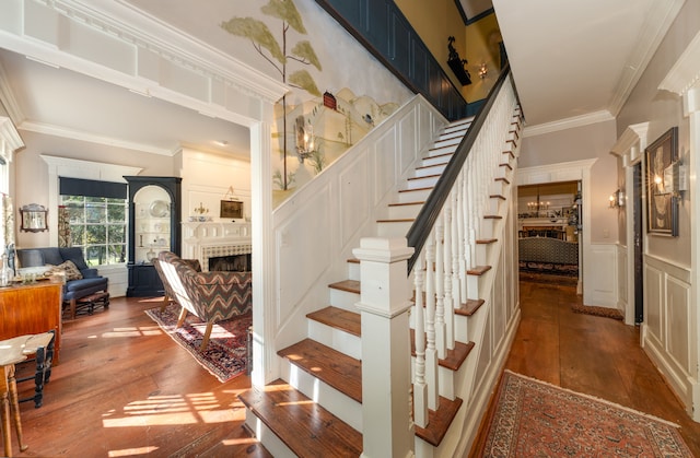 stairway with a tile fireplace, wood-type flooring, and crown molding