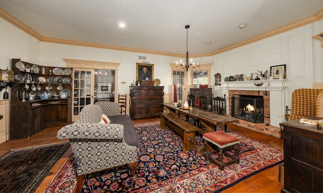 living room with hardwood / wood-style floors, a notable chandelier, ornamental molding, and a brick fireplace