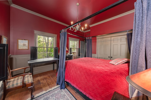 bedroom featuring a closet, wood-type flooring, crown molding, and an inviting chandelier