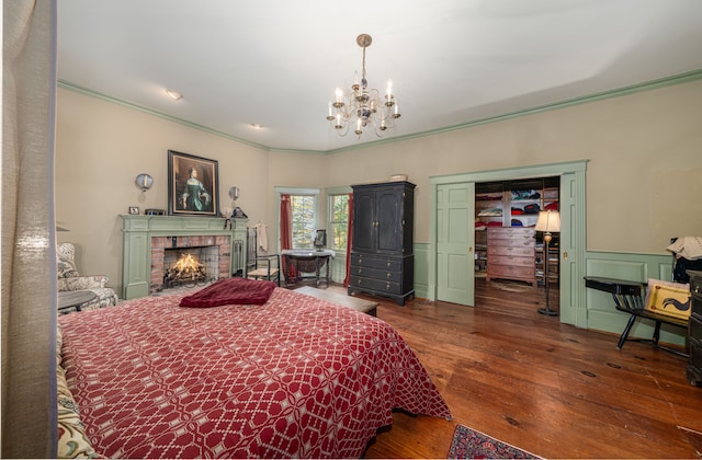 bedroom with a fireplace, crown molding, dark hardwood / wood-style flooring, and an inviting chandelier