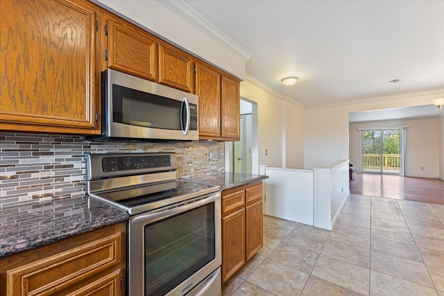 kitchen featuring backsplash, dark stone counters, light tile patterned floors, ornamental molding, and appliances with stainless steel finishes