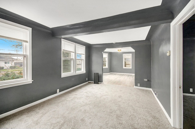 carpeted empty room with beam ceiling, radiator, and plenty of natural light