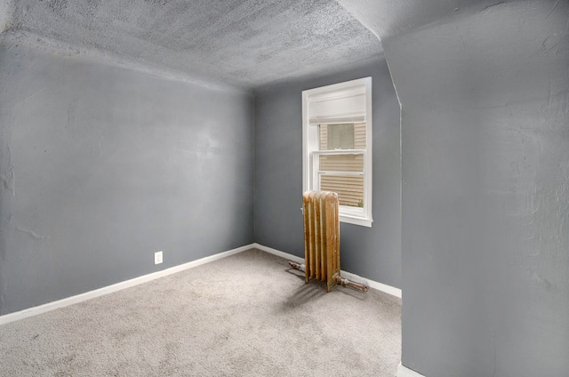 carpeted empty room featuring radiator and a textured ceiling