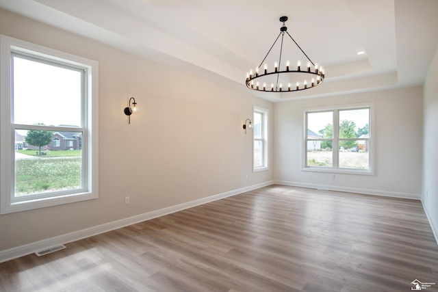 unfurnished room featuring hardwood / wood-style flooring, a tray ceiling, and a notable chandelier