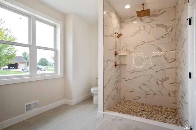 bathroom with toilet, plenty of natural light, and tiled shower