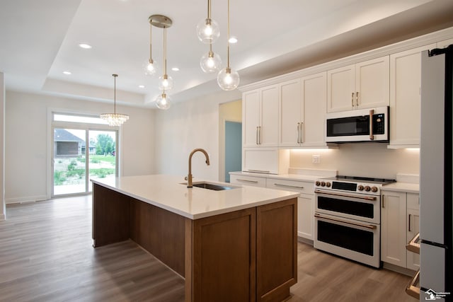 kitchen with double oven range, white cabinets, a center island with sink, sink, and decorative light fixtures