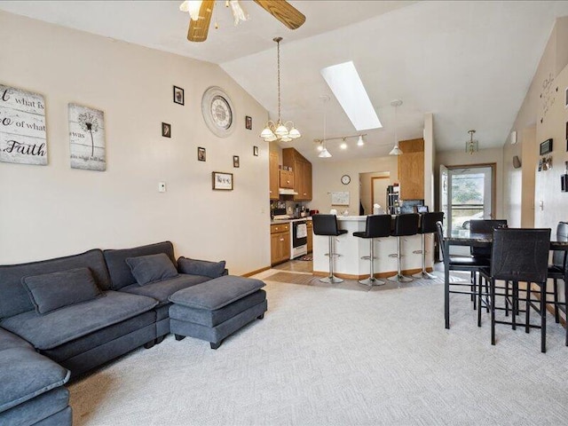 carpeted living room featuring ceiling fan with notable chandelier and lofted ceiling with skylight