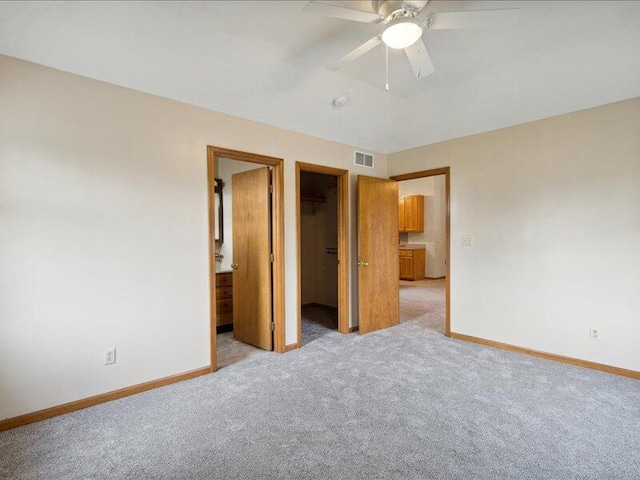 unfurnished bedroom featuring a walk in closet, ceiling fan, a closet, and light carpet