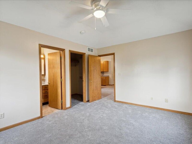 unfurnished bedroom with light carpet, a spacious closet, a closet, and ceiling fan